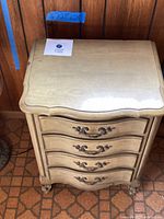 Front view of the hardwood nightstand showing the four curved drawers with ornate metal handles and carved feet.