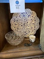Photo showing blue and white Passover plate, white Seder cups, small glass whale, and Waterford crystal bowl placed inside a wooden cabinet.