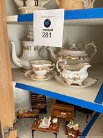 Shelf with white and gold bone china tea pot, cup and creamer, sugar dish with lid, showing the set and detailing
