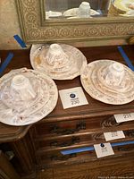 Three complete 5-piece place settings of floral ceramic dinnerware stacked with cups inverted on top, placed on wooden furniture under a mirror.