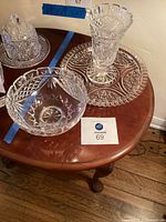 Three Waterford crystal pieces displayed on wooden table: vase, serving bowl, and dish with lid.