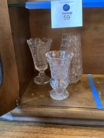 Three crystal vases displayed together inside a wooden cabinet shelf showing size and shape variation.