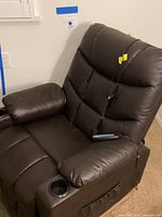 Front and side view of the brown leather recliner showing padded armrests with integrated cup holder and attached remote control cord.