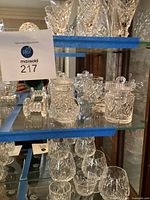 Shelf with crystal items including jam/jelly holders and dumbbell decoration, with auction tag visible.