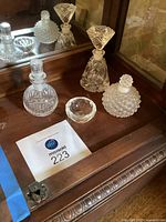 All four items (three perfume bottles and ring dish) on wooden surface with mirror
