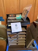 Metal wall-mounted 3-hole punch alongside the 6-shelf paper storage unit with some boxes and supplies placed on top