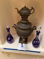 Full view of the antique metal samovar with two blue crystal bottles on either side placed in recess.