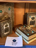 Four silver-clad volumes on wooden shelf with turquoise accents