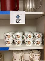 Twelve bone china coffee cups arranged on a shelf showing floral patterns and curved handles.