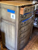 Side and front view of six drawer dresser showing pale green color, curved drawer fronts with metal handles, and upper drawer partially opened.
