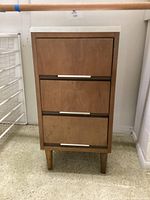 Front view of wooden three drawer table with brass handles and white top.