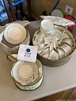 Overview of the tea set including stacked dessert plates, a pile of teacups with paper wrapping, and stack of saucers, alongside quilted storage cases.