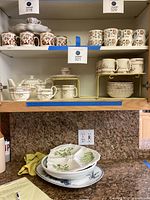 Shelves display coffee cups with floral patterns, stacked plates, and matching saucers in yellow and brown floral design.