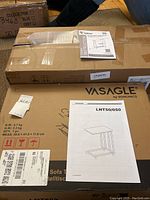 Photo of unopened Vasagle box with instruction manual on top, showing model LNT50/050 sofa table with wheels.