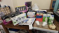Overview of assorted light bulbs and smart lighting devices on a table, including multiple brands and types of bulbs, some in packaging, some loose.
