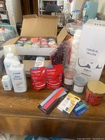Photo shows unopened cervical pillow box, Colgate Wisp packs, baby powder bottles, cotton balls, various candles, nail files and other small personal care products arranged on a wooden table.
