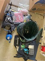Image displaying various camping items on floor including stadium seats, trash bin, cookware, utensils, and accessories.