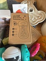 Close-up of DerYEP Dog Crate Training Toy packaging, bone-shaped treat puzzle, and several chew toys including a light green one and a pink spiked ring.