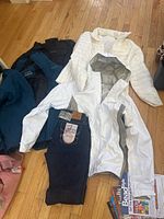 Photo showing assorted jackets including white Columbia jacket with gray panels and white quilted jacket along with black and blue jackets and dark denim flame-resistant jeans.