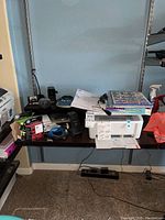 Full view of desk shelf with HP LaserJet Pro MFP M31w printer, Dymo label maker, pencil sharpener, DVI-D cable, ink cartridges, and user manuals scattered on the desk surface and shelf.