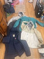 Five jackets displayed on the floor showing various colors and styles including beige and teal jackets with hoods and a navy blue puffer jacket.