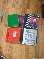 Eight assorted left-handed notebooks and drawing pad arranged on wooden floor