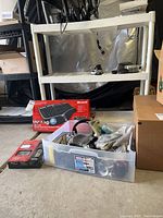 Wide view of plastic bin on floor with various computer accessories, Microsoft keyboard box, and additional packaging boxes nearby.
