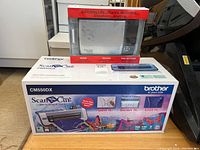 Side view of Brother ScanNCut CM550DX box with Flip-Pal mobile scanner box on top, showing product details and branding.