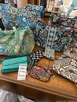 Overview of Vera Bradley bags and wallets on wooden table showing various floral and paisley patterned quilted fabric bags and wallets in multiple colors