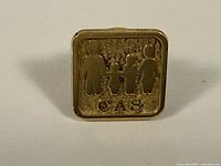 Front view of gold pin showing two adults holding hands with two children and letters 'C A S' beneath.