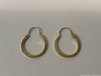 Top view of both gold hoop earrings on white background, showing etched pattern and hinged latch closure