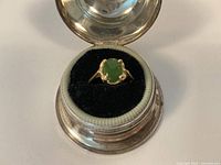 Ring displayed front-facing in round metal case with black velour interior