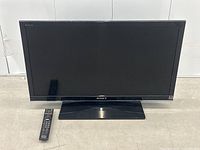 Frontal photo of Sony Bravia TV showing entire screen and remote laid beside it on the floor.