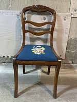 Front view of antique wooden chair with blue floral needlepoint seat showing carved backrest and floral detail