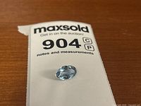Blue topaz gemstone placed on auction tag showing lot number 904 for identification and size context.