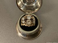 Top-down view of ring in round presentation box showing six diamonds and filigree setting