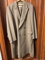 Full view of tan Aquascutum wool overcoat on hanger, showing the double-breasted front and flap pockets