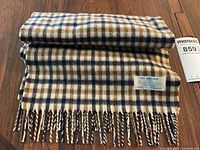 Folded wool scarf with check pattern and fringe on hardwood floor