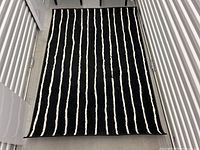 Full view of black and white striped area rug laid flat, showing vertical irregular white stripes on black background, photographed in a storage setting.
