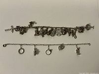 Overview photo showing both charm bracelets laid flat, one chunky with many charms, the other delicate with a few heart-themed charms.