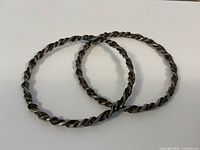 Two twisted rope sterling silver bangles lying flat on a white surface, showing circular shape and twisted design.