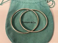Two interlocked sterling silver bangles displayed on Tiffany & Co teal pouch