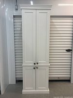 Front view of the two-piece white wall cabinet, showing the full height with four paneled doors and stone knob handles.