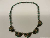 Full view of the vintage green necklace showing bead and decorative metal segments.