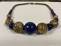 Close-up front view of vintage cobalt blue and gold tone textured bead necklace showing central large blue stone bead and surrounding gold tone beads.