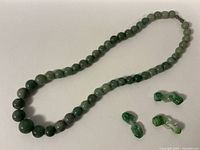 Full view of the jade beaded necklace laid out with the three jade carved pieces beside it on a white background.