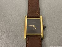 Front view of rectangular gold-plated case, black dial with Cartier logo, gold-tone hands
