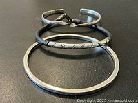 Three sterling silver bracelets and bangles on black background, showing twisted cuff with strap, slim engraved bangle, and thick hammered bangle