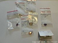 Seven small plastic bags each containing a single loose faceted gemstone of various colors, identified as beryl, amethyst, and citrine with handwritten carat weights on bags.