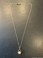 Full view of gold chain necklace with teardrop pendant and pearl on black background